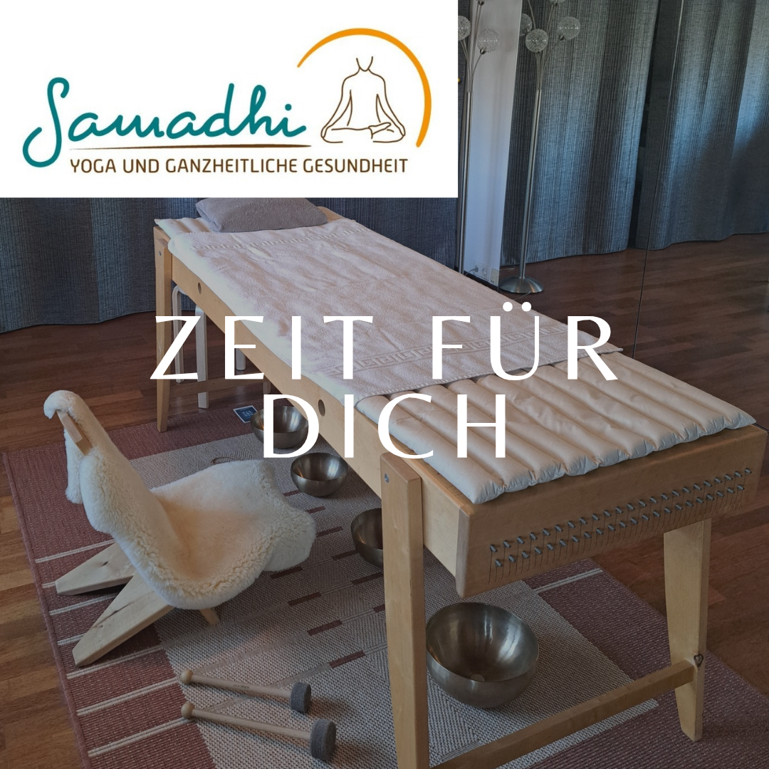 Ein Holzmassagetisch mit Handtuch, Kissen und Schüsseln auf einem Teppich. Ein weißer Stuhl und ein Yoga-Studio-Logo sind in der Nähe. Die Worte 'Zeit fur Dich' sind über dem Tisch geschrieben.