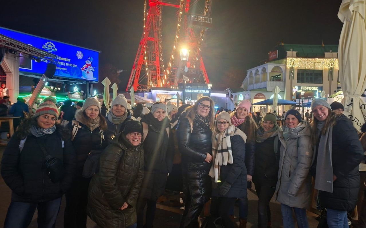 Eine Gruppe von Frauen in Winterkleidung steht nachts vor einem großen beleuchteten Turm und lächelt für ein Foto.