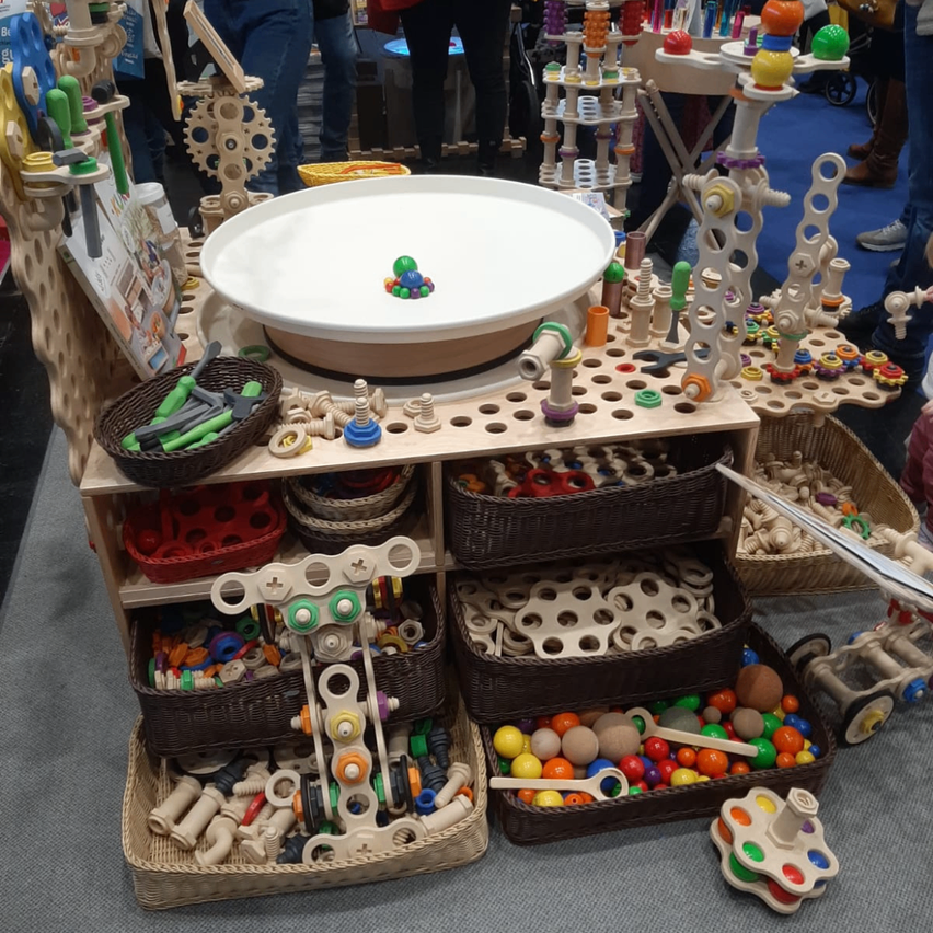 Ein Holzwagen mit mehreren Körben und Tabletts voller bunter Spielzeuge. Eine große weiße Schüssel befindet sich in der Mitte.