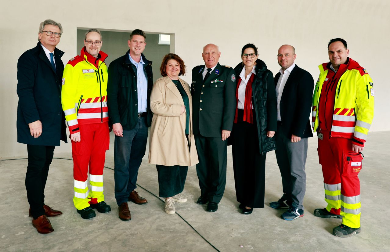 Eine Gruppe von Personen in formeller Kleidung, einschließlich eines Militäroffiziers, steht lächelnd für ein Foto in einem Raum.