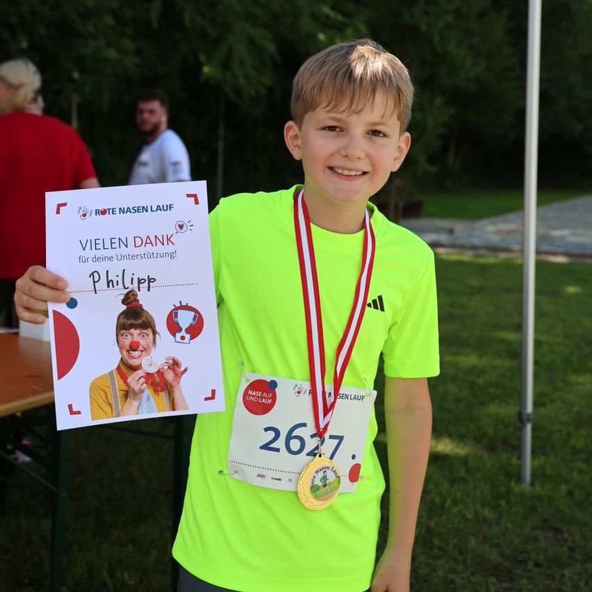 Ein Junge mit einer Medaille um den Hals hält ein Zertifikat, auf dem steht Vielen Dank für deine Unterstützung! Philipp.