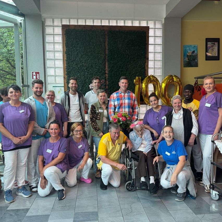 A group of people, including staff and patients, are posing for a photo in a well-lit room with balloons and decorations.