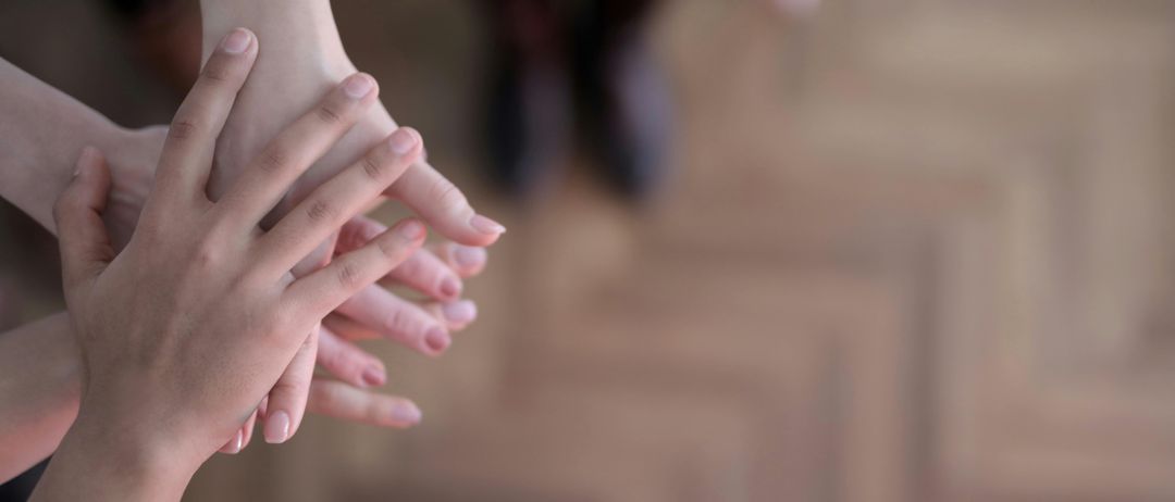 Ein Nahaufnahme von Händen, die Einheit zeigen, wobei die Finger einer Hand mit denen einer anderen verflochten sind, vor einem unscharfen hölzernen Bodenhintergrund.