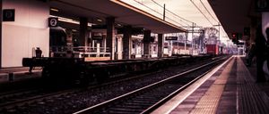 Ein Bahnhof im Freien mit Bahnsteig, Oberleitungen und einem Zug auf der Strecke.