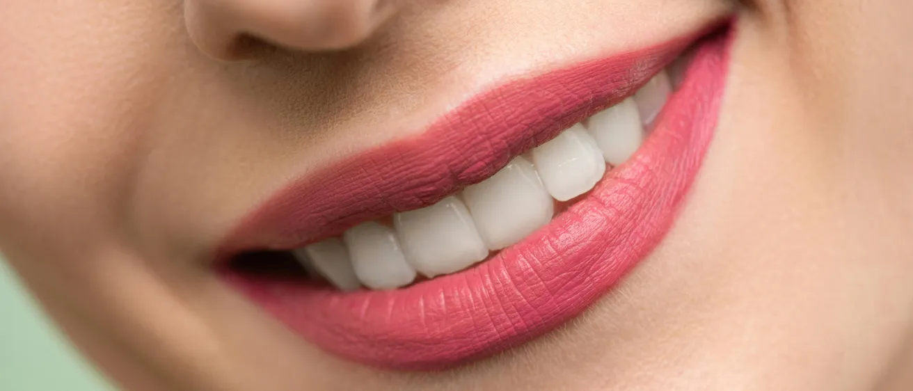 Ein Nahaufnahme des Gesichts einer Frau mit rosa Lippenstift und weißen Zähnen.