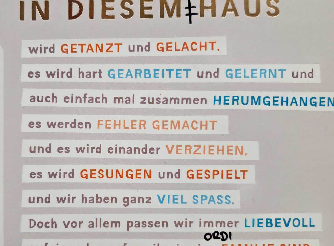 Ein Plakat mit verschiedenen Phrasen auf Deutsch. Oben steht 'IN DIESEM+HAUS'. Darunter sind Phrasen wie 'wird GETANZT und GELACH,' 'es wird hart GEARBEITET und GLERNT' und 'es werden FEHLER GEMACHT.' Das Plakat betont Familienliebe und Einheit.