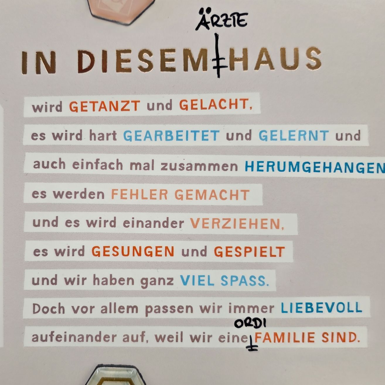 Ein Plakat mit verschiedenen Phrasen auf Deutsch. Oben steht 'IN DIESEM+HAUS'. Darunter sind Phrasen wie 'wird GETANZT und GELACH,' 'es wird hart GEARBEITET und GLERNT' und 'es werden FEHLER GEMACHT.' Das Plakat betont Familienliebe und Einheit.