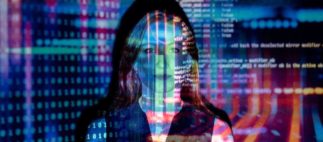 Eine Frau steht vor einem farbenfrohen, digitalen Hintergrund, der mit Binärcode und Programmiersprache gefüllt ist. Ihr Gesicht ist teilweise durch farbige Linien und Text verdeckt.