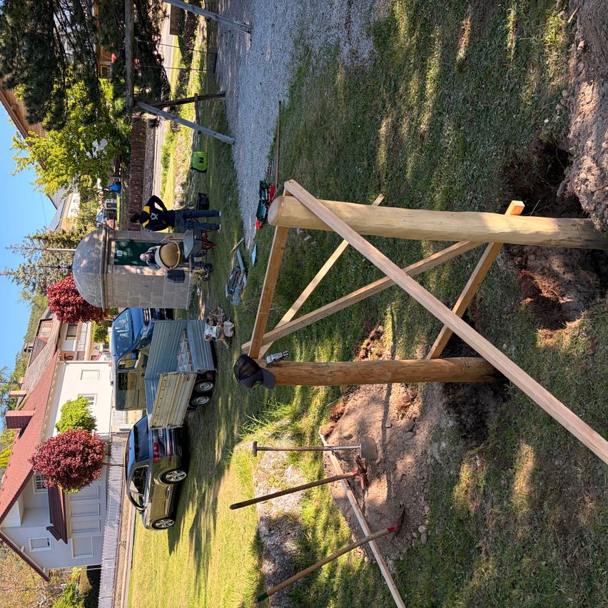 Eine Vogelperspektive einer Holzkonstruktion in Bau auf einem Rasenfeld, umgeben von geparkten Fahrzeugen und einem Gebäude.