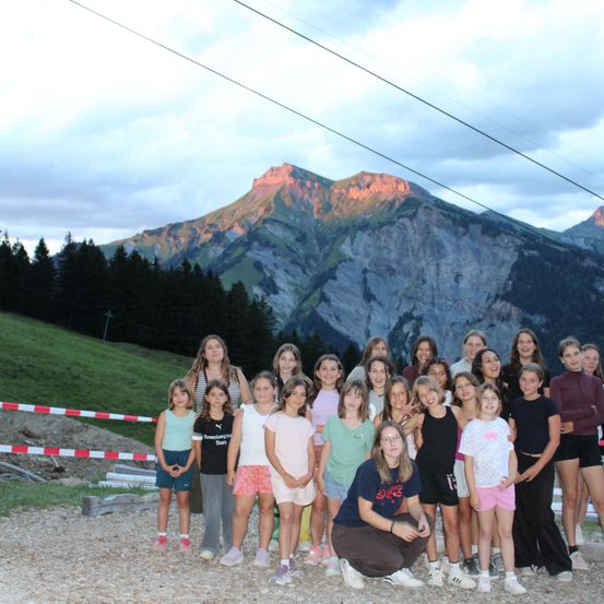 Eine Gruppe junger Mädchen und Frauen posiert für ein Foto vor einem Berg mit bewölktem Himmel.