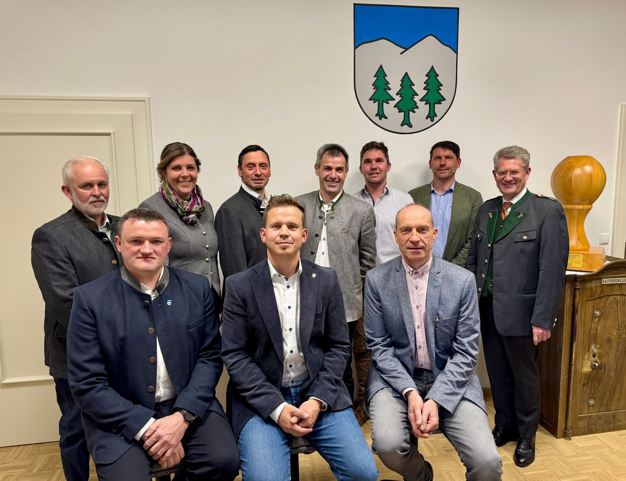 Eine Gruppe von Männern und Frauen in formeller Kleidung posiert für ein Foto vor einer Wand mit einem Wappen.