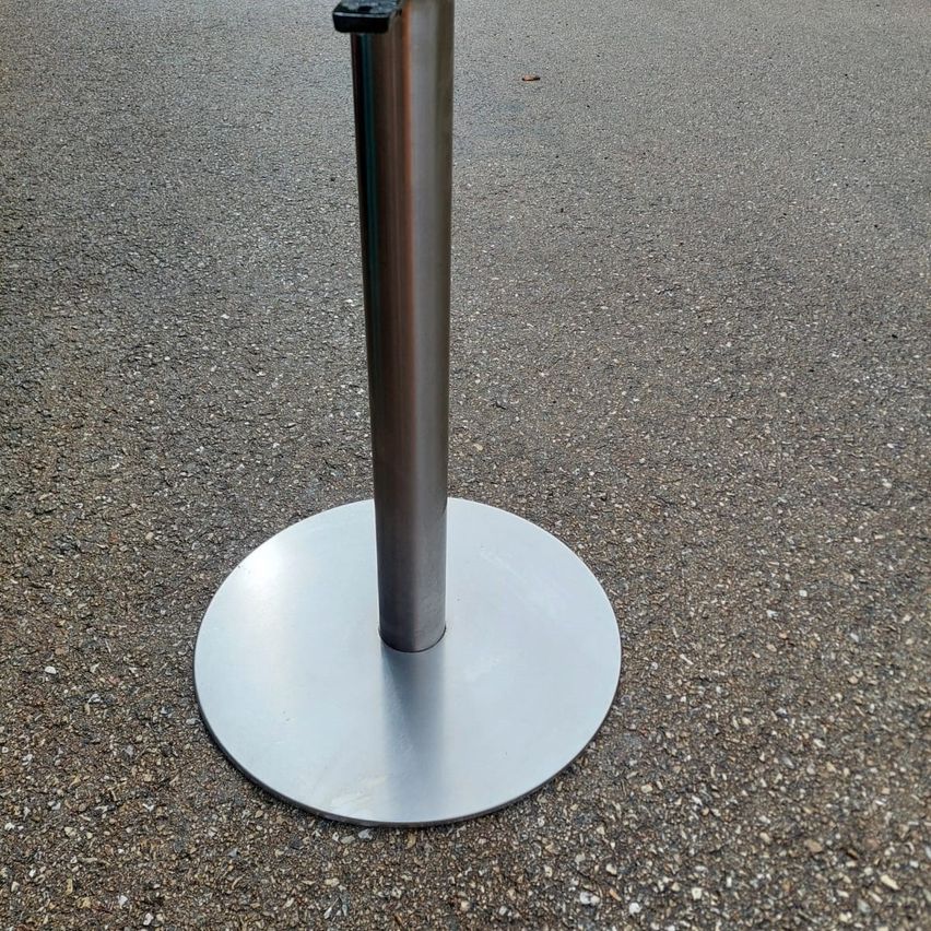 Ein Edelstahlfuß mit runder Basis steht auf einer Betonoberfläche.