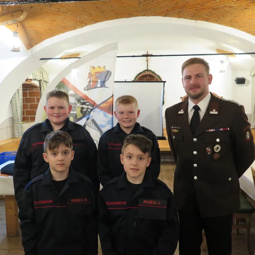 Fünf junge Jungen in schwarzen Uniformen mit roten Streifen posieren für ein Foto. Ein Mann in Uniform steht vor ihnen.