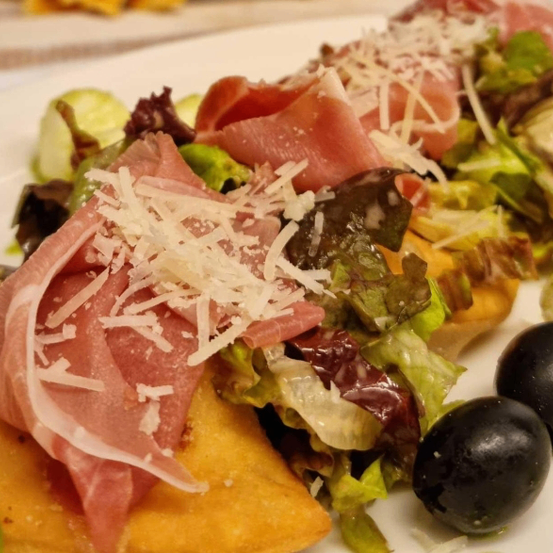 Ein Teller mit Salat, geschnittenem Fleisch, Käse und Oliven auf einem weißen Teller.