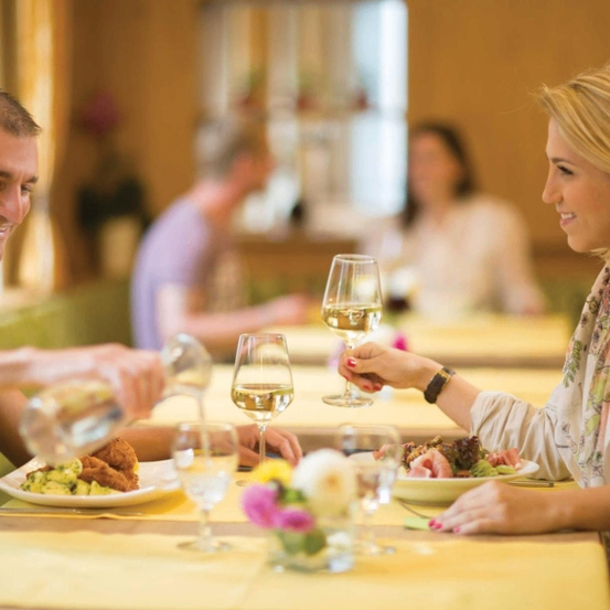 Ein Mann schenkt einer Frau Wein in ein Glas ein, während sie in einem Restaurant mit anderen dinieren.