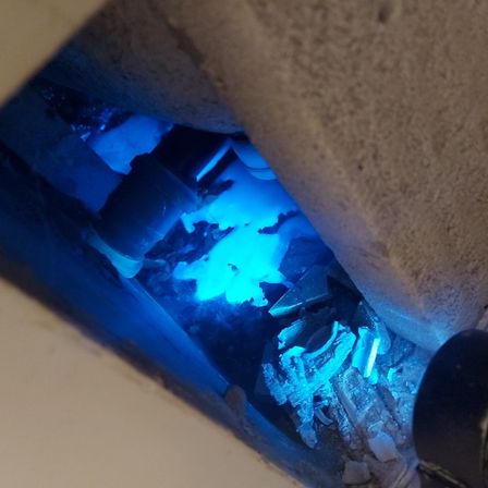 Ein dunkler Raum mit einem blauen Licht, das zerbrochenes Glas und Rohre zu beleuchten scheint.