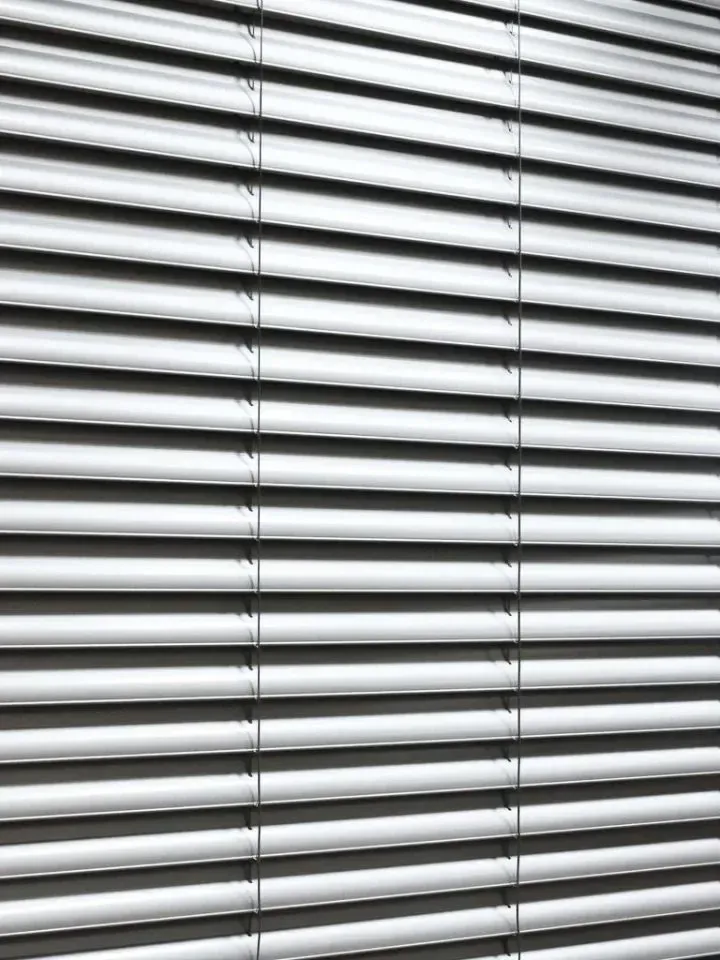 Ein Nahaufnahme von weißen horizontalen Jalousien, ordentlich angeordnet und gefaltet, die ein elegantes und organisiertes Erscheinungsbild erzeugen.
