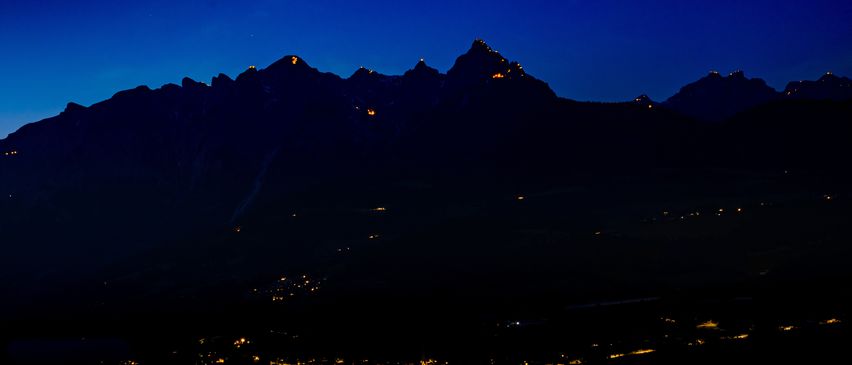 Ein Nachtblick auf Berge mit beleuchteten Gipfeln und einer Stadt unten.
