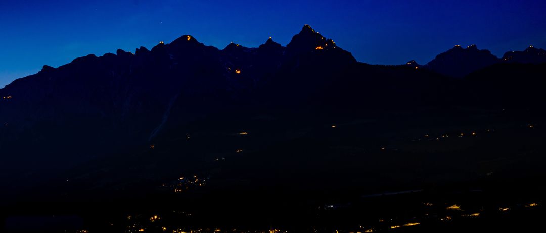 Ein Nachtblick auf Berge mit beleuchteten Gipfeln und einer Stadt unten.