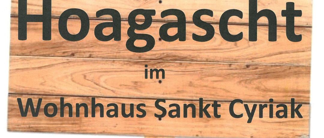 Ein Holzschild zeigt 'Hoagascht im Wohnhaus Sankt Cyriak'. Darunter steht 'Erster Mittwoch im Monat um 13:30 Uhr'. Weiter unten heißt es 'Wir freuen uns auf Ihren Besuch'.