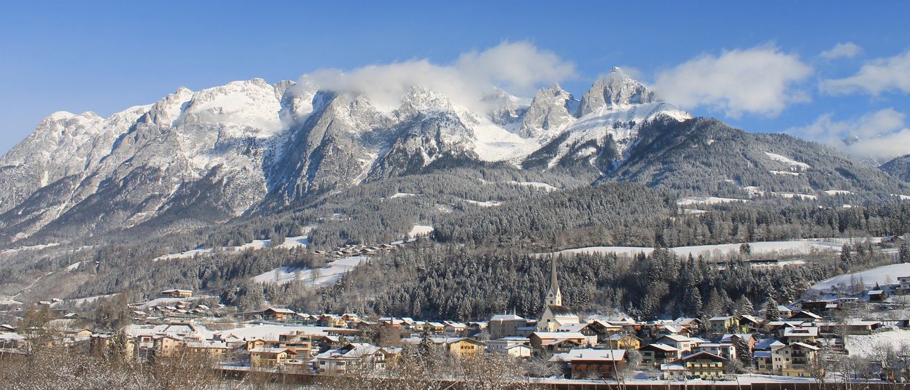 Ein Panoramablick auf eine verschneite Berglandschaft mit einer Stadt darunter unter einem klaren blauen Himmel.