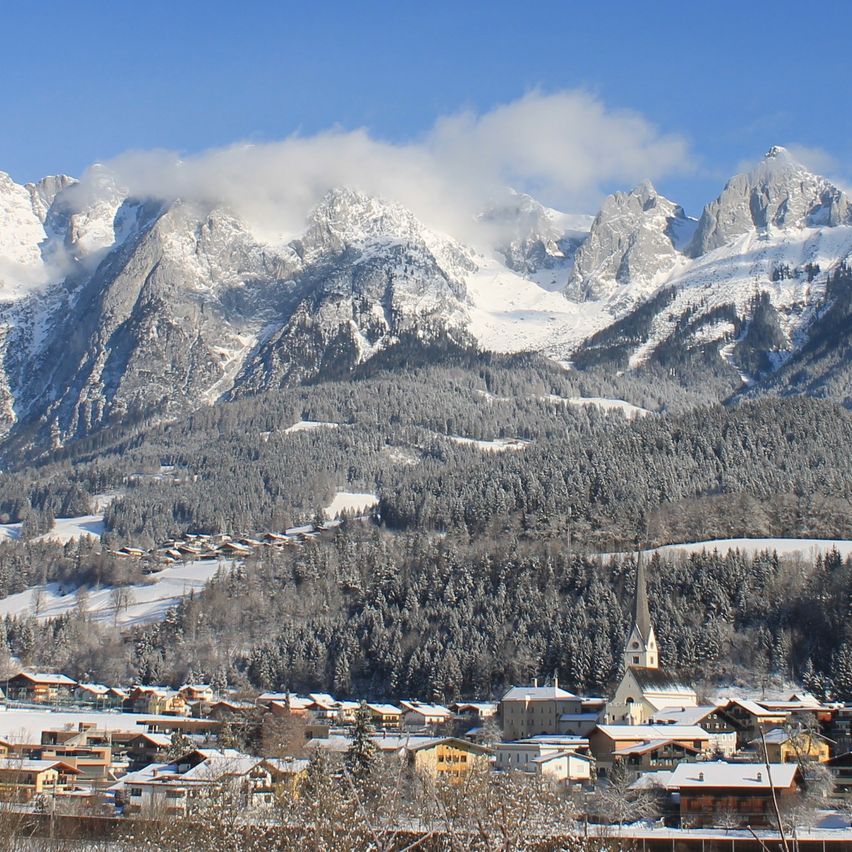 Ein Panoramablick auf eine verschneite Berglandschaft mit einer Stadt darunter unter einem klaren blauen Himmel.
