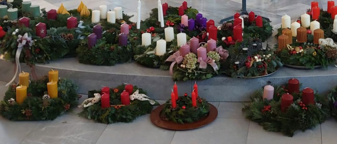 Eine Reihe von Kränzen, geschmückt mit verschiedenfarbigen Kerzen, grünen Blättern und Tannenzapfen, auf Betonstufen.