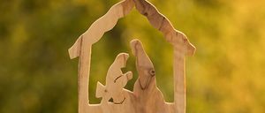 Eine hölzerne Krippe mit Maria und Josef im Inneren, vor einem unscharfen grünen Hintergrund dargestellt.