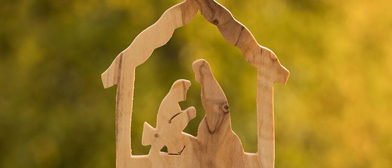 Eine hölzerne Krippe mit Maria und Josef im Inneren, vor einem unscharfen grünen Hintergrund dargestellt.