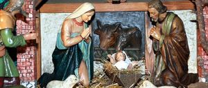Eine Krippenszene mit Maria, Josef und dem Baby Jesus in einer Stallung, umgeben von Tieren und Felsen.