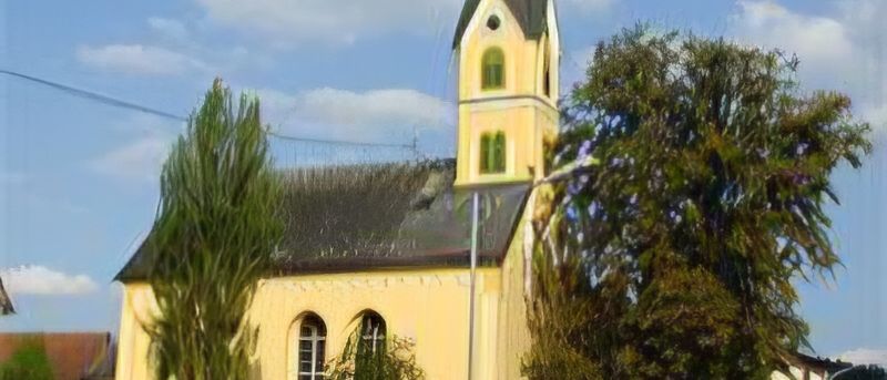 A yellow church with a steeple and green windows stands under a blue sky with clouds. Trees surround the church.