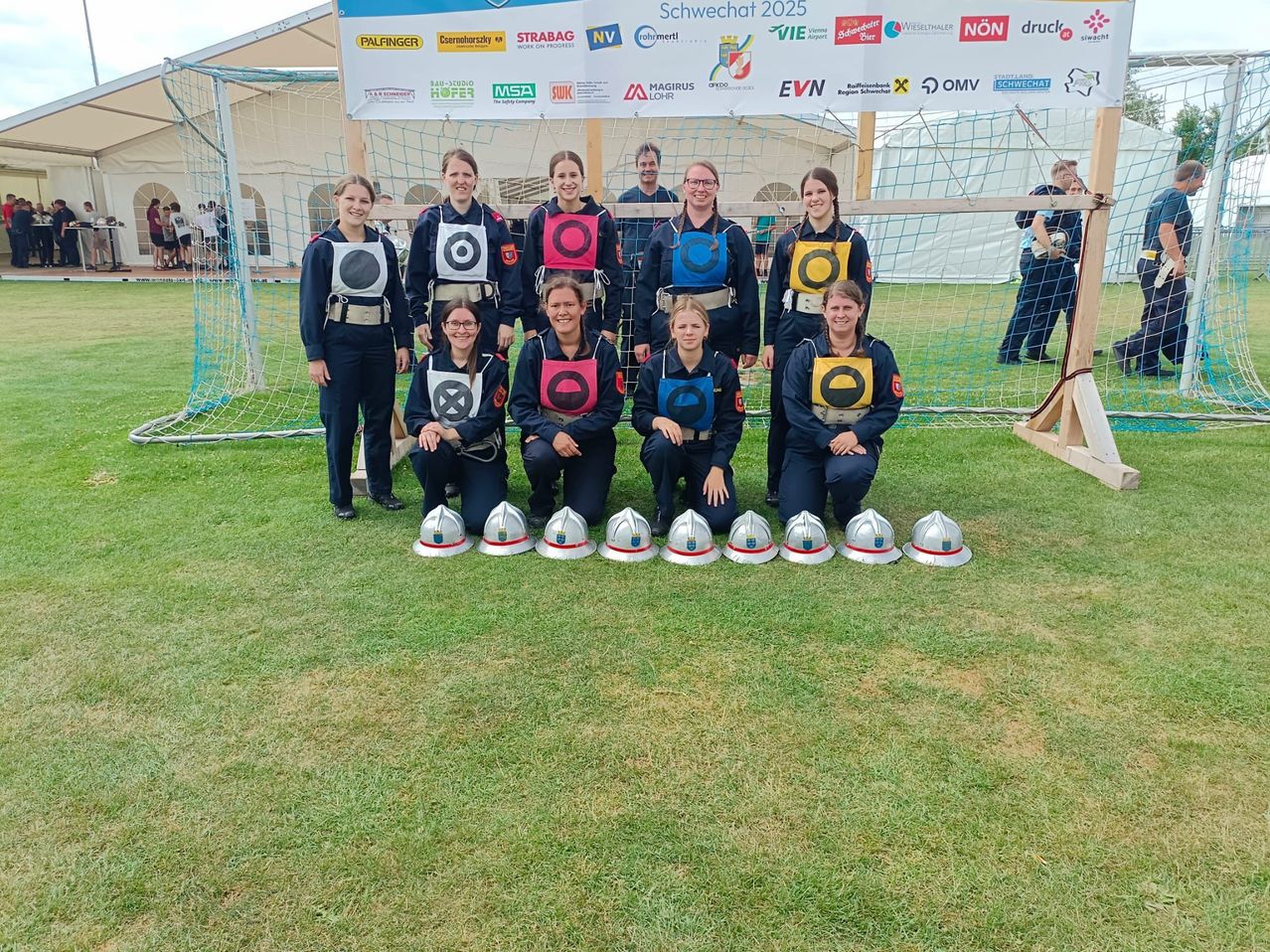 Eine Gruppe von Frauen in Uniform posiert vor einem Tor für ein Foto, trägt Westen mit Zielen und Helme auf dem Boden.