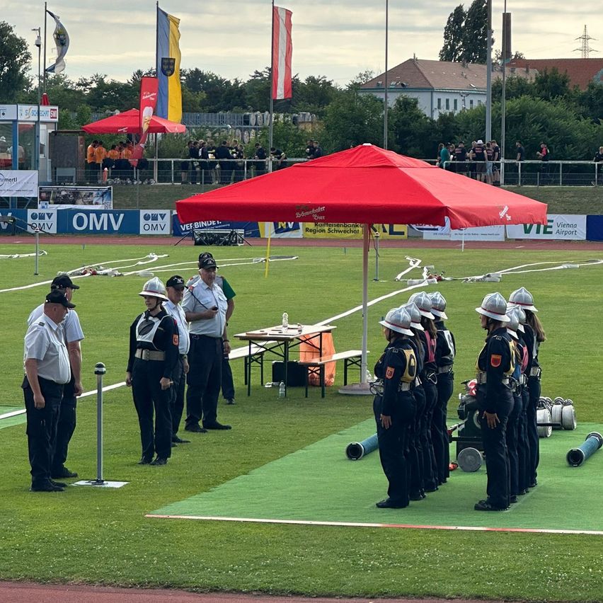 Eine Gruppe uniformierter Beamter steht auf einem Feld unter einem roten Zelt, mit Ausrüstung und Bannern im Hintergrund.