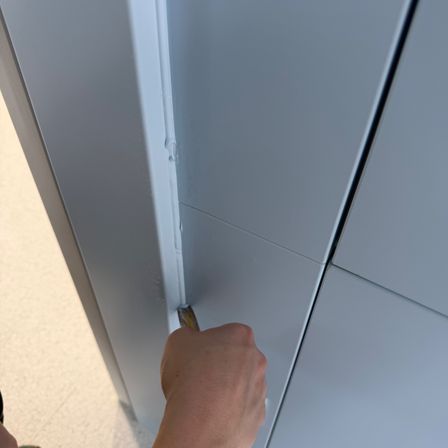 Eine Hand benutzt ein Werkzeug, um die Naht zwischen zwei weißen Paneelen einer Struktur anzupassen. Die Paneele sind Teil einer gebogenen Oberfläche.