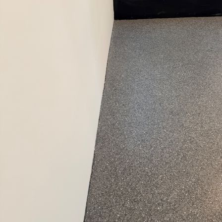 Eine Ecke eines Raums mit einer weißen Wand, die auf einen grauen Teppich trifft. Der Teppich ist fleckig und sieht sauber aus.