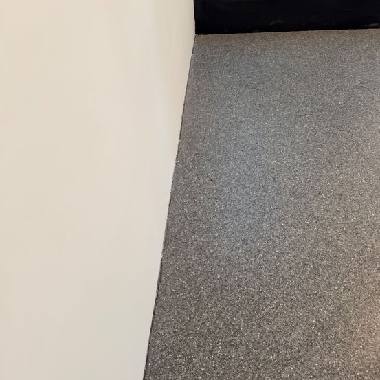 Eine Ecke eines Raums mit einer weißen Wand, die auf einen grauen Teppich trifft. Der Teppich ist fleckig und sieht sauber aus.