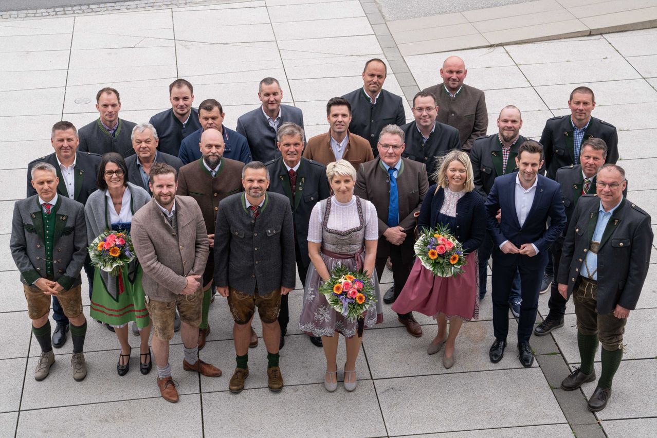 Eine Gruppe von Erwachsenen, sowohl Männer als auch Frauen, gekleidet in traditioneller Kleidung und Geschäftsanzügen, steht auf einem Betonboden und posiert für ein Foto.