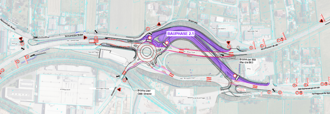 A detailed urban planning map showing a roundabout with labeled roads, bridges, and construction phases. The map includes various colored lines and annotations.
