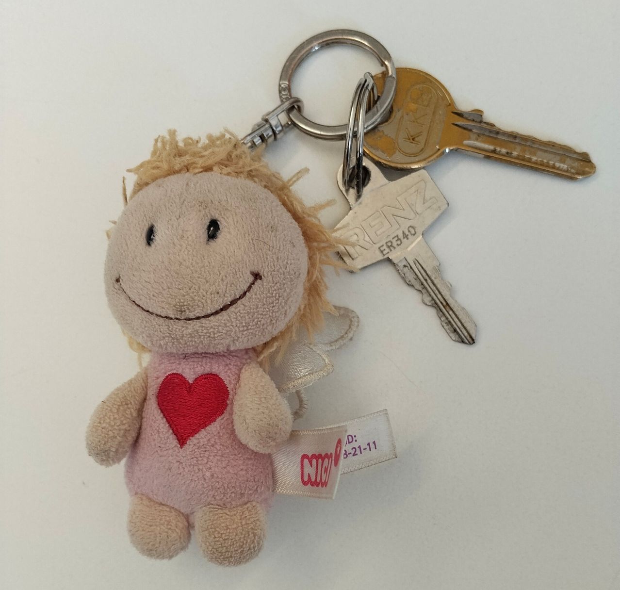A small plush doll with blonde hair and a pink shirt with a red heart on it. The doll is attached to a keyring with two keys labeled 'RENZ' and 'ER340'.