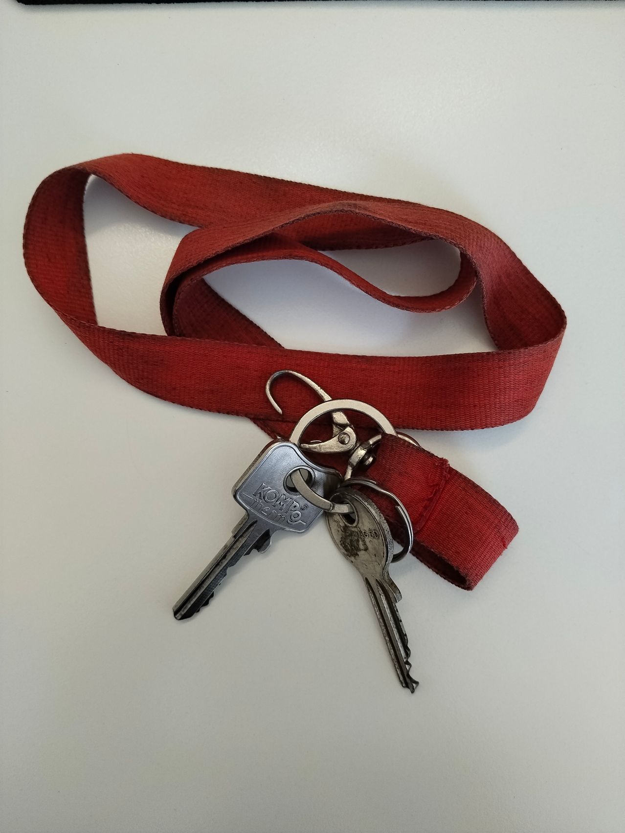 Ein roter Schlüsselanhänger mit zwei Schlüsseln, einer mit dem Wort Kombi, ist auf einer weißen Oberfläche zu sehen.