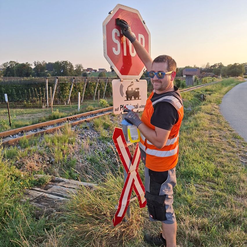 Ein Mann in einer orangenen Weste malt ein Stoppschild in der Nähe einer Eisenbahnstrecke.