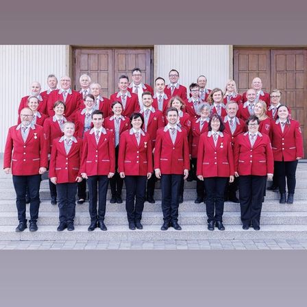 Ein Chor in roten Blazern und schwarzen Hosen posiert auf Stufen vor einem Gebäude.