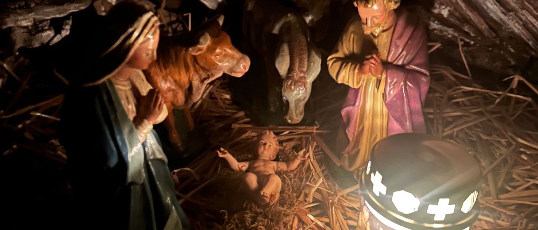 Eine Krippe mit Maria, Josef und Baby Jesus, ausgestellt in einer schwach beleuchteten Höhle mit einer Kerze in der Nähe.