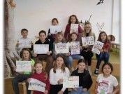 Eine Gruppe von Kindern und Jugendlichen posiert für ein Bild, während sie Schilder hochhalten und in die Kamera lächeln. Sie sitzen auf Bänken.