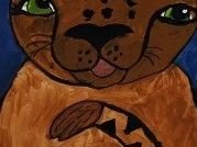 Eine braune Katze mit grünen Augen und schwarzen Flecken hält eine Nuss. Die Katze hat eine rosa Zunge und schaut geradeaus.
