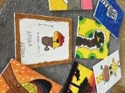 Eine Sammlung kleiner, bunter Gemälde ist auf einer grauen Oberfläche platziert. Jedes Gemälde zeigt verschiedene Tiere, darunter ein Giraffe, ein Vogel, einen Wurm und eine Katze.