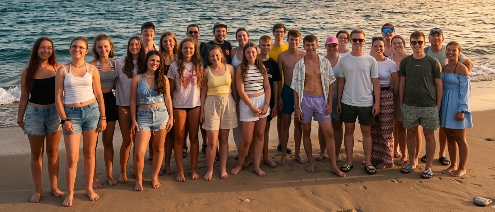 Eine Gruppe von Menschen in lässiger Strandkleidung posiert für ein Foto auf einem sandigen Strand bei Sonnenuntergang.