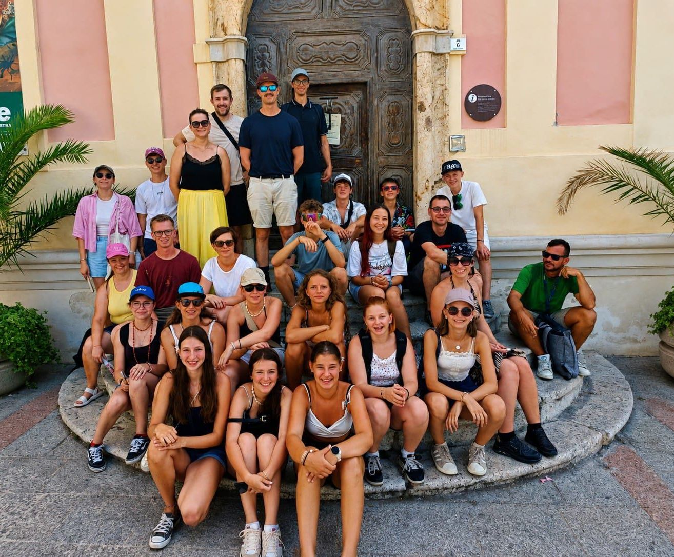 Eine Gruppe von Männern und Frauen posiert für ein Foto vor einem alten Gebäude mit einer Holztür und einer Plakette an der Wand.