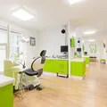 Das Innere einer Zahnklinik mit grünem Thema. Es verfügt über Zahnarztstühle, Schränke und einen Monitor an der Wand.