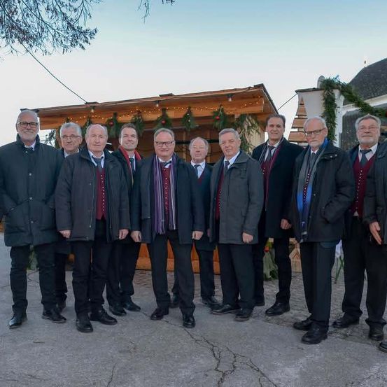 Eine Gruppe von Männern in Anzügen und Krawatten steht zusammen vor einem hölzernen Gebäude mit Dekorationen.
